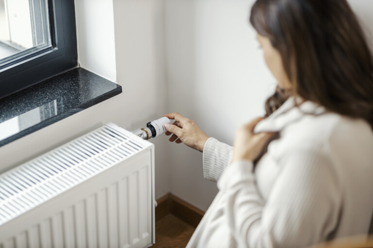 A pregnant woman is turning heating up on radiator at her apartment.